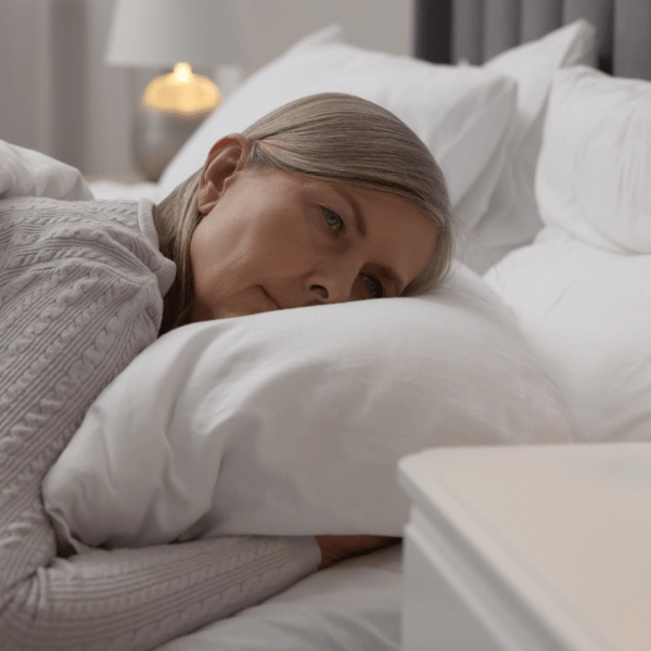 Older woman lying awake in bed, looking thoughtful and concerned, representing sleep difficulties during menopause.