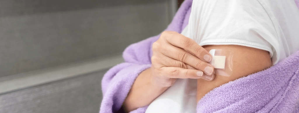 Woman&rsquo;s hand applying a hormone patch to her upper arm, representing hormone therapy as a treatment option in menopause.