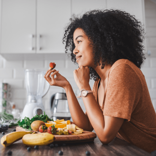 Woman pausing before eating, holding a strawberry and practicing mindful eating with fresh fruit on the table.