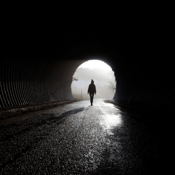 Silhouette of a person walking toward a bright light at the end of a dark tunnel, symbolizing healing, hope, or emergence from mental darkness.