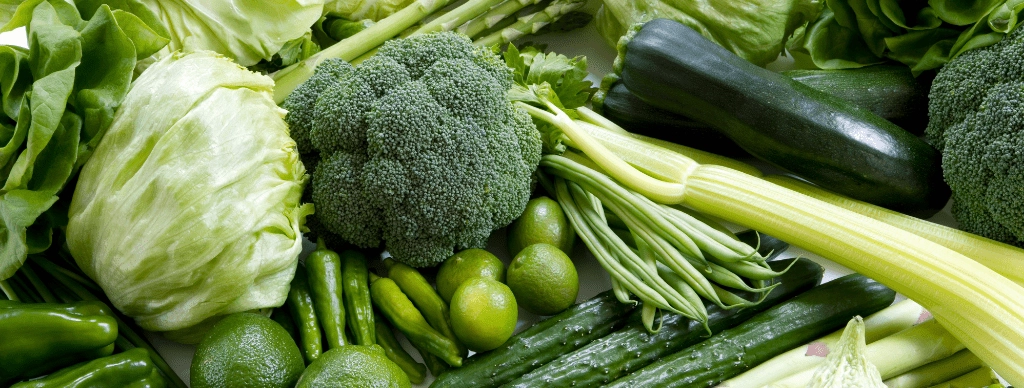 Assortment of fresh green vegetables including lettuce, broccoli, zucchini, celery, and green beans, representing a nutrient-rich, healthy diet for optimal wellness.