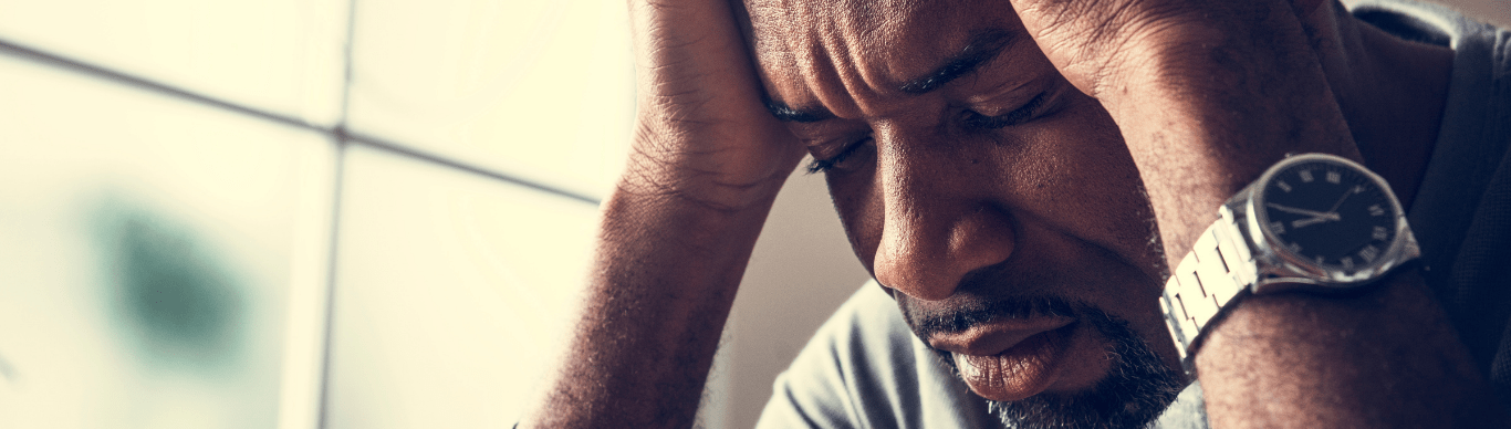 Stressed man sitting by a window with his head in his hands, illustrating the connection between light, mood, and mental health.