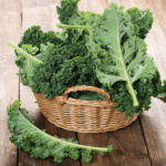 A woven basket filled with fresh, leafy green kale, placed on a rustic wooden table.