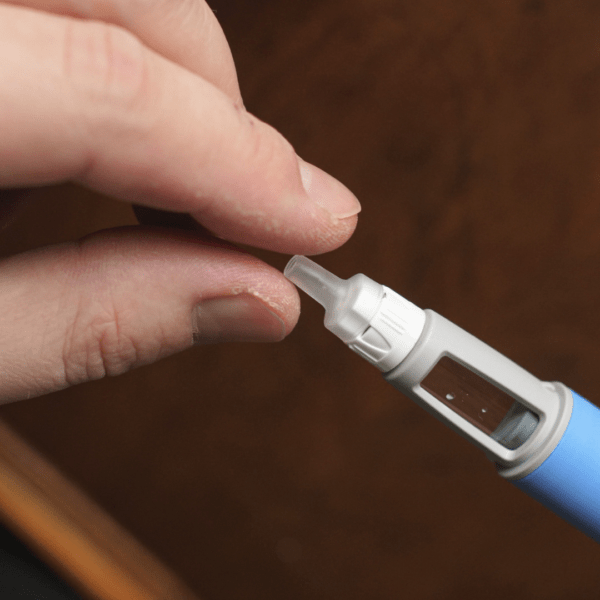 Close-up of fingers attaching a needle cap to a blue GLP-1 injection pen, demonstrating safe medication preparation.