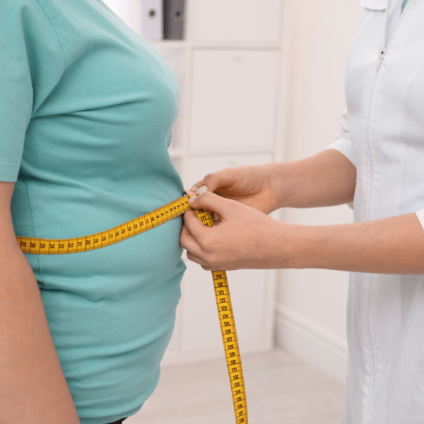 Healthcare professional measuring a patient’s waist circumference with a yellow tape measure, illustrating clinical assessment for obesity or weight loss.