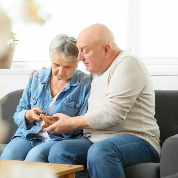 An elderly couple sitting together while the woman pricks her finger.