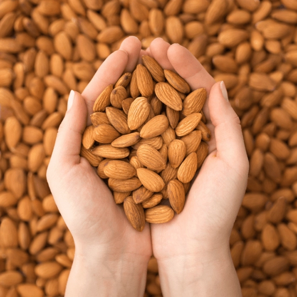 Two hands holding a handful of raw almonds with more almonds