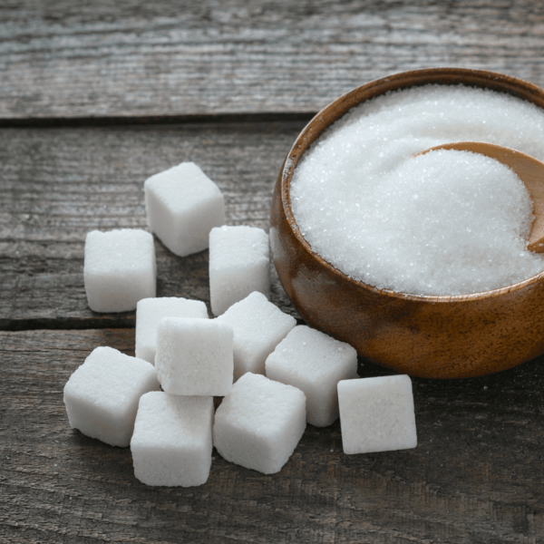 A wooden bowl filled with white granulated sugar and surrounded by sugar cubes on a rustic wooden surface.