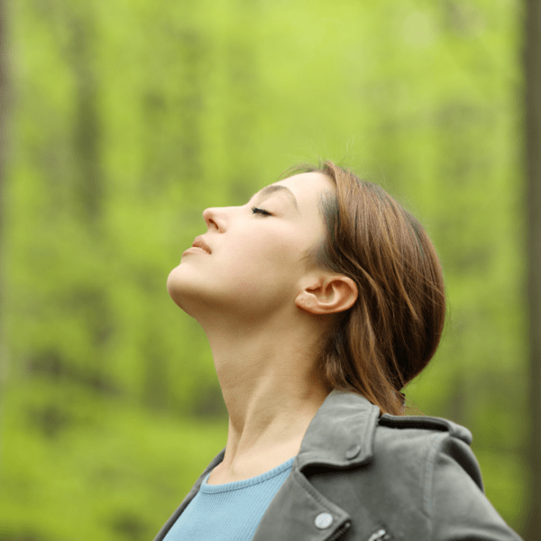 Peaceful woman outdoors with eyes closed, taking a mindful breath surrounded by spring greenery.