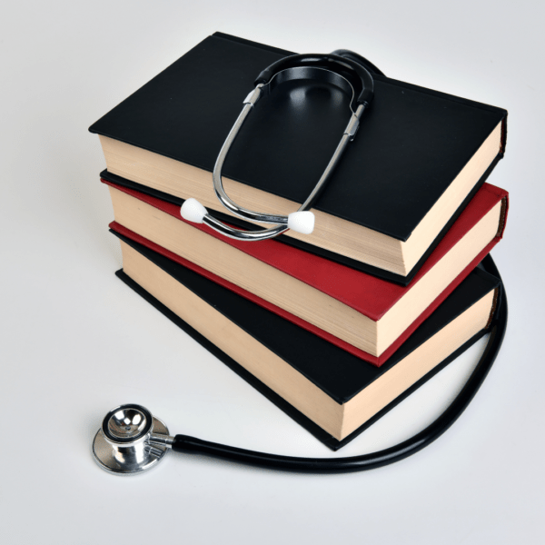 A stack of thick medical textbooks with black and red covers lies on a white surface, topped with a stethoscope, symbolizing medical education and study.