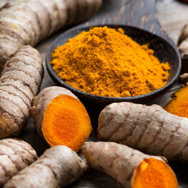 A close-up of turmeric root and ground turmeric powder in a wooden bowl, highlighting its vibrant orange color and natural texture.