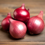 A group of glossy red onions on a wooden surface, showcasing their deep red color and smooth texture.