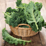 A woven basket filled with fresh, leafy green kale, placed on a rustic wooden table.