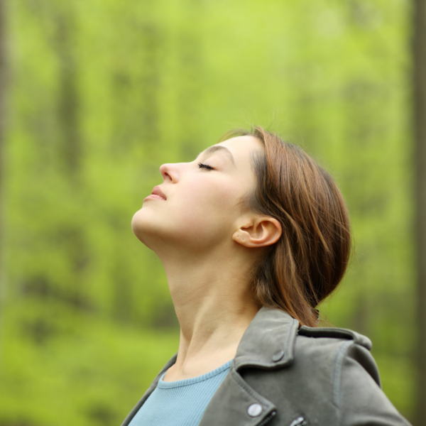 Peaceful woman outdoors with eyes closed, taking a mindful breath surrounded by spring greenery.