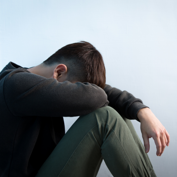 Young man sitting on the floor with head buried in his arms, expressing emotional pain, depression, or the impact of unresolved trauma.