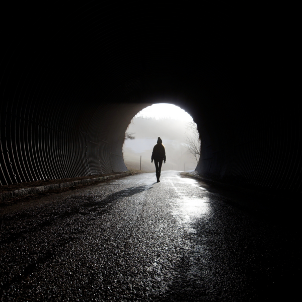 Silhouette of a person walking toward a bright light at the end of a dark tunnel, symbolizing healing, hope, or emergence from mental darkness.