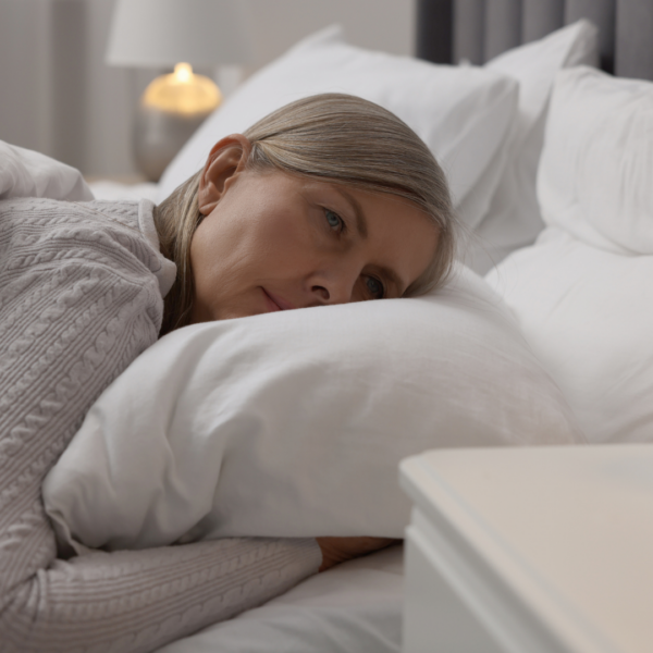 Older woman lying awake in bed, looking thoughtful and concerned, representing sleep difficulties during menopause.
