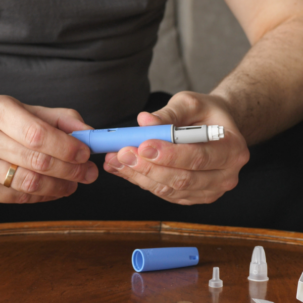 Person assembling a blue GLP-1 injection pen, preparing for weekly medication injection, with cap and supplies on the table