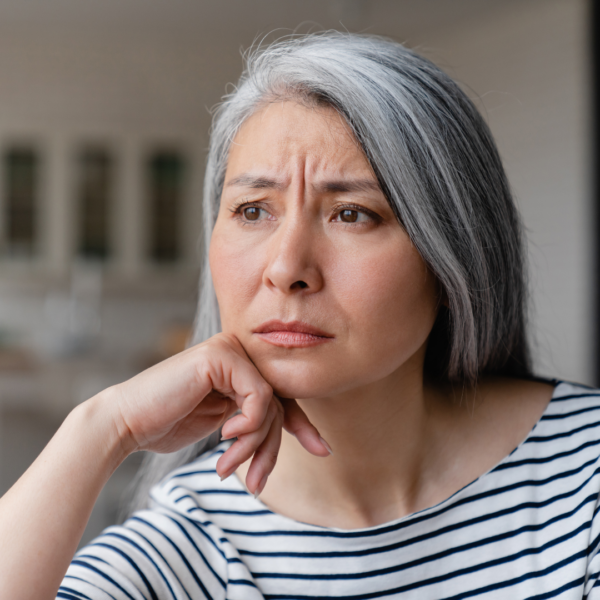 Middle-aged woman with gray hair sitting at home, resting her chin on her hand and appearing pensive, reflecting emotional changes in midlife.