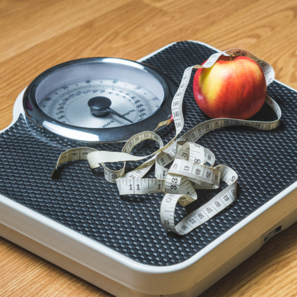 Analog bathroom scale with a measuring tape and a red apple on top, representing healthy weight loss and tracking progress.