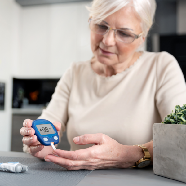 Mature woman checking her blood sugar level at home, illustrating the connection between hormones, insulin, and metabolic health.