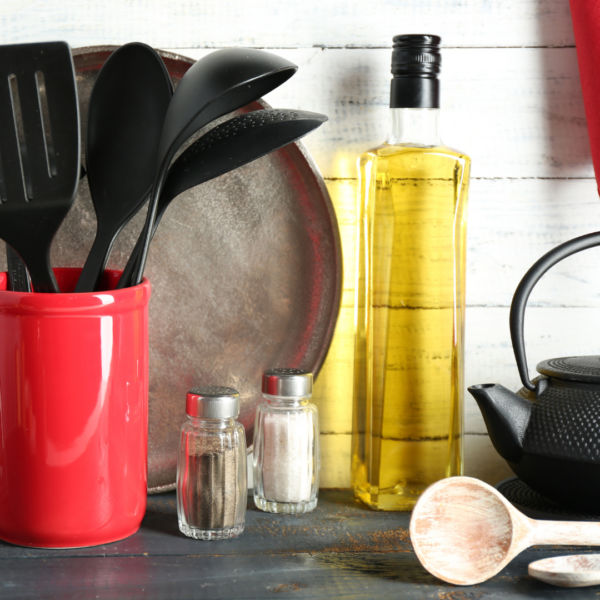 Kitchen countertop with cooking utensils in a red holder, salt and pepper shakers, a bottle of vegetable oil