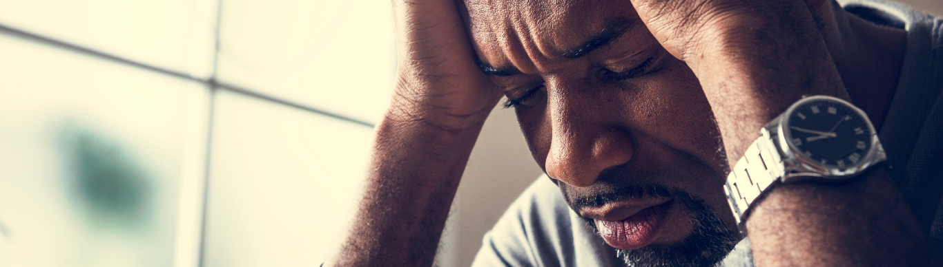 Stressed man sitting by a window with his head in his hands, illustrating the connection between light, mood, and mental health.